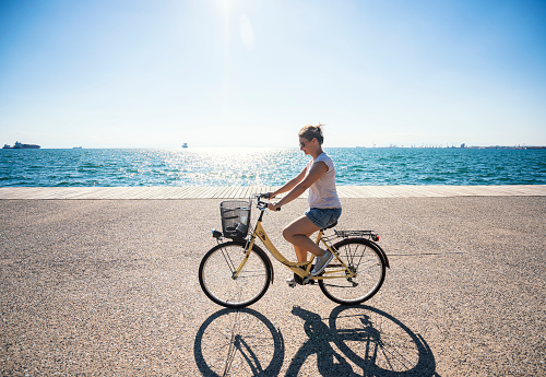 Woman riding bicycle on the promenade along the seaside