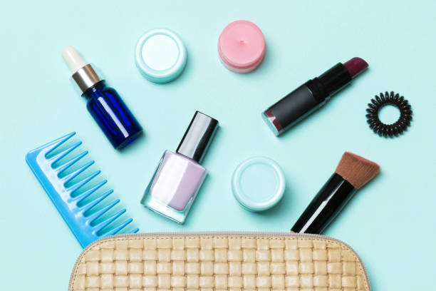 top view of set of make up and skin care products spilling out of cosmetics bag on blue background. beauty concept - pampering nail polish make up spilling imagens e fotografias de stock