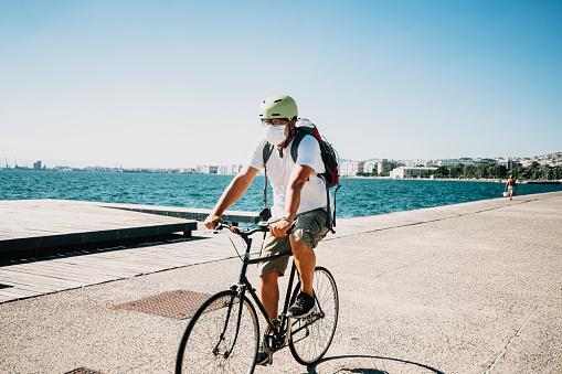 Man riding bicycle on the promenade along the seaside, wearing face mask