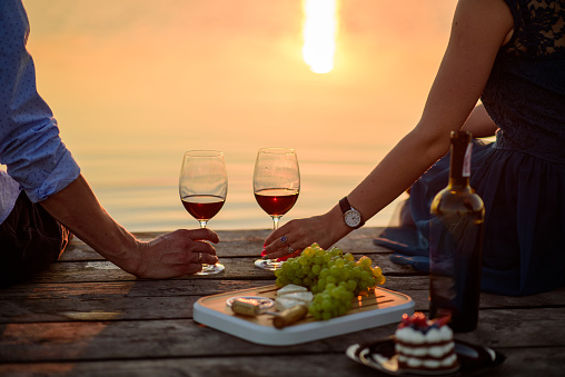 Man and woman clanging wine glasses on the background of colorful summer sunset