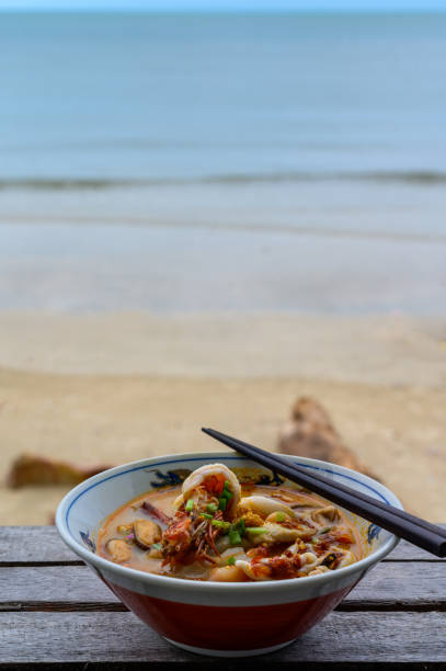 River prawn spicy soup or Tom yum kung in bowl on wooden table on beach near sea
