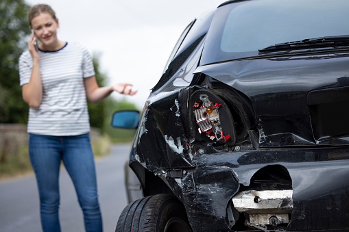 Conductor femenino infeliz con el coche dañado después del accidente llamando a la compañía de seguros en el teléfono móvil photo
