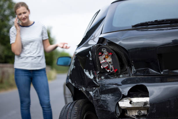 携帯電話で保険会社に電話する事故の後、損傷した車を持つ不幸な女性ドライバー - dented ストックフォトと画像