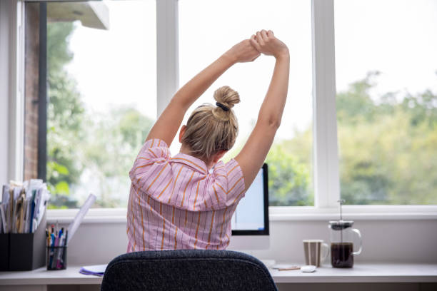 visão traseira da mulher trabalhando em casa no computador em home office esticando na mesa - stretching - fotografias e filmes do acervo