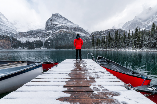 Man traveler standing on wooden pier with red canoe and snowing in Lake O'hara at Yoho national park, Canada