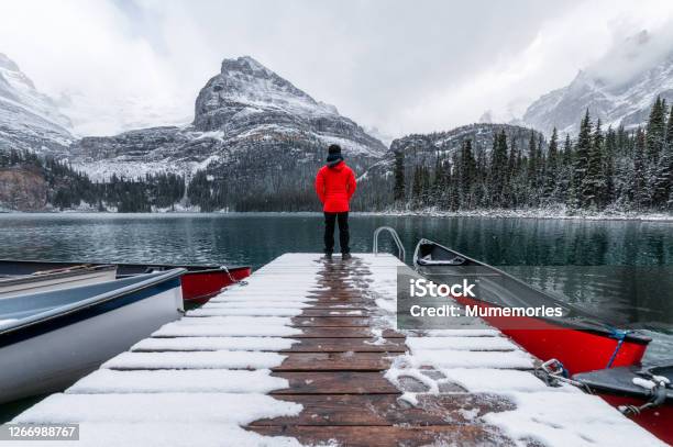Man Traveler Standing On Wooden Pier With Red Canoe And Snowing In Lake Ohara At Yoho National Park Stock Photo - Download Image Now