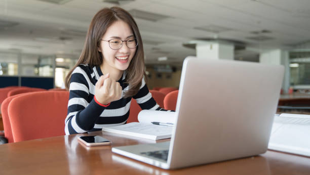 de volta à escola de conhecimento universitário conceito universitário, linda estudante sorridente usando serviço de educação on-line, jovem olhando em laptop exibição assistindo treinamento e escuta - registo livro - fotografias e filmes do acervo