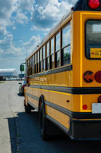 Rear left view of a school bus behind a car under a cludy blue sky