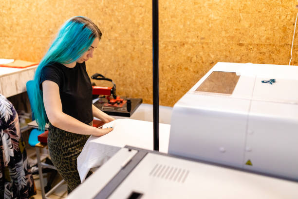 skoncentrowana miejska młoda kobieta przygotowuje biały t-shirt na jedwabnej maszynie do prasowania do druku - printing plant printing press digitally generated image textile industry zdjęcia i obrazy z banku zdjęć