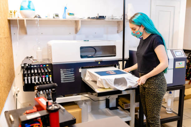 現代の女性労働者は、シルクスクリーン印刷機でtシャツを印刷した結果を見て、彼女は結果に驚いています - printout ストックフォトと画像