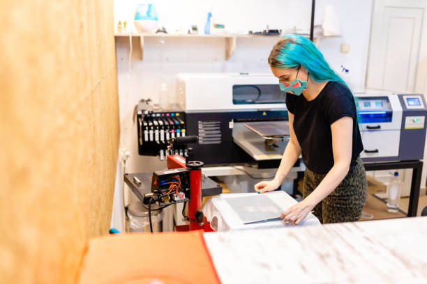 istock In digital printing workshop female worker preparing T-shirt for printing while wearing protective face mask during COVID-19 pandemic 1266995057
