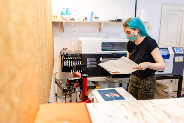 istock Responsible female worker wearing protective face mask while printing T-shirt with a help of technology 1266995096