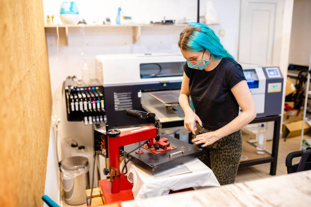 nowoczesna pracownica za pomocą maszyny do prasowania, aby mogła nałożyć nadruk na bawełniany t-shirt - printing plant printing press digitally generated image textile industry zdjęcia i obrazy z banku zdjęć