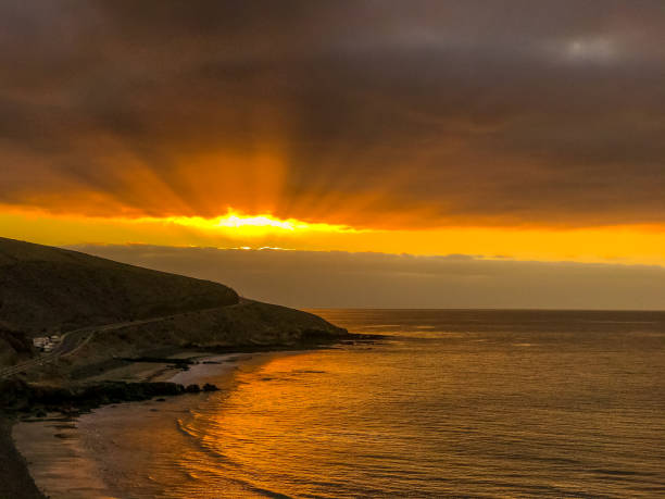 istock Sunrise from a cliff with moving clouds in a different direction forming a line where the sun rises on the sea and forms rays reflecting on the ocean surface from the Grand Canary. 1266995812