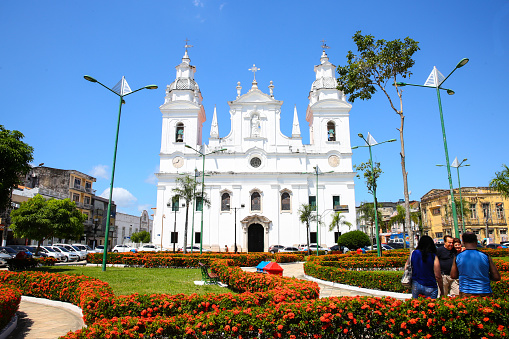 Famous church in the city of Belém do Pará in Brazil. This beautiful church was built in 1755 when Brazil was a colony of Portugal. Its name is Famous church in the city of Belém do Pará in Brazil. This beautiful church was built in 1755 when Brazil was a colony of Portugal. Its name is Igreja da Sé or Nossa Senhora da Graça do Pará and it is one of the secular constructions of Belém. and it is one of the secular constructions of Belém. A blue sky and a garden with red flowers frame the church. Many tourists like these in the photo talk and choose the best angles for a photo.