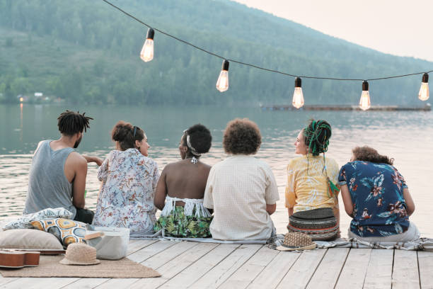 Rear view of group of friends sitting on a pier and talking to each other they enjoying the nature