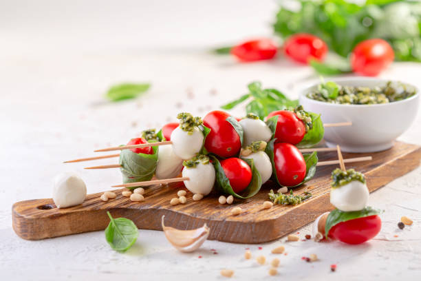 Caprese salad on skewers with pesto sauce. Caprese salad-mozzarella, basil, cherry tomatoes, pesto sauce, skewers. Italian homemade food and a healthy diet concept. caprese salad stock pictures, royalty-free photos & images