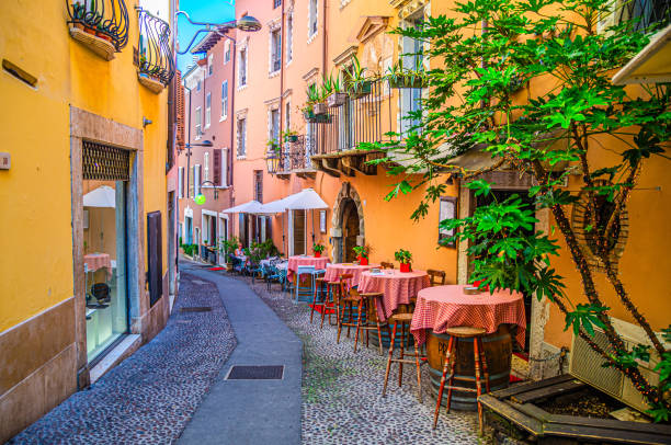 Desenzano del Garda, Italy, September 11, 2019: restaurant tables on wooden barrels and chairs in typical italian narrow street and traditional colorful buildings in old historical town centre