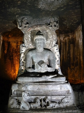 An ancient dilapidated stone statue of the Buddha inside a dark hall of a rock cut cave temple at Ajanta.