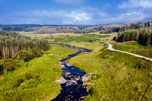 The view from a drone of a small river and dirt road in an open area of pine forest in Scotland.\nThe river runs into a large Scottish loch that is used for a hydro electric scheme.
