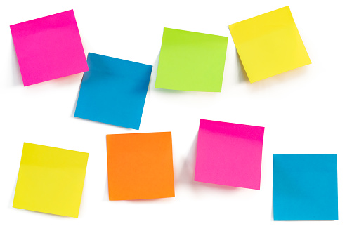 Yellow, green, blue, orange and magenta colored sheets of a adhesive booklet on a white wall. Close up. Space for ideas or messages.