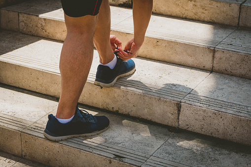 Male runner tying his shoes preparing for a jogging at staircase in city public park.