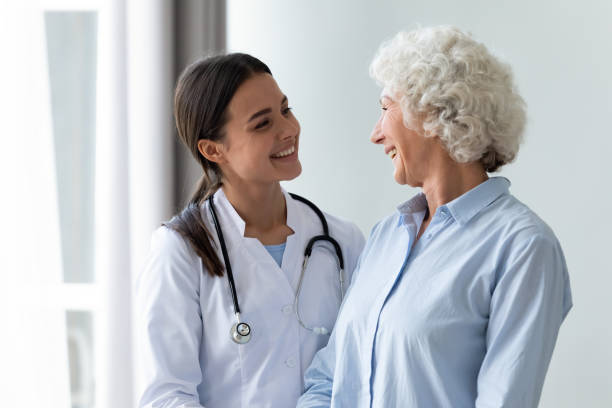 Caring millennial nurse helping middle aged patient at meeting. Smiling young female general practitioner enjoying sincere talk, sharing good health news with hoary older senior woman indoors. Caring millennial nurse helping middle aged patient at meeting. doctor stock pictures, royalty-free photos & images