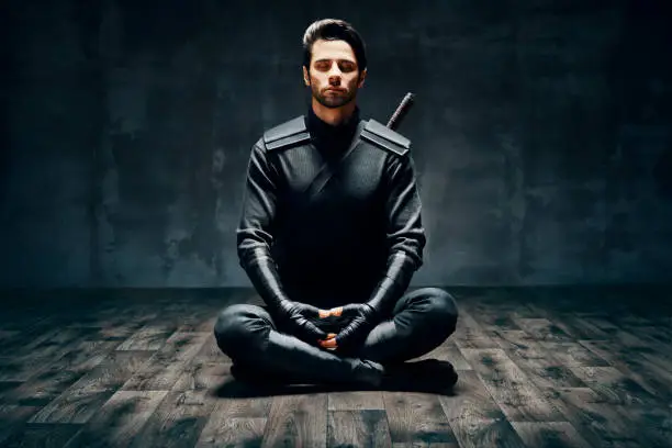 Warrior man meditating in Lotus pose over black background