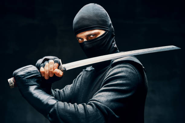Fighting ninja posing with a sword over black background stock photo