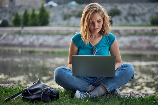 Beautiful teenage girl enjoying a day by the city river, using a laptop computer.