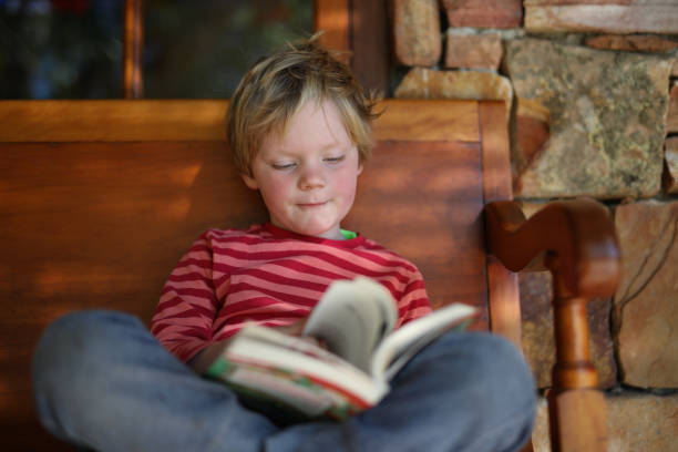 istock A young boy sitting on a wooden bench while reading a book. 1267019854