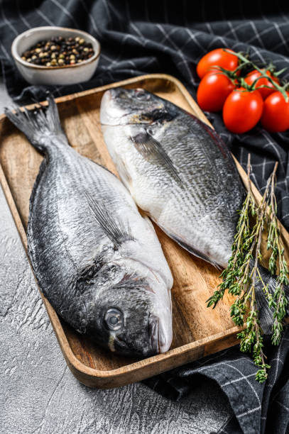 istock Raw sea bream fish with cooking ingredients, cherry tomatoes, thyme, pepper. Gray background. top view 1267022408