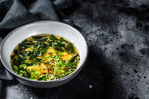 Hot miso soup in a bowl. Black background. Top view. Copy space.