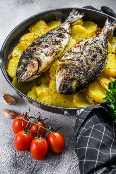 istock Grilled sea bream fish with potatoes in a pan. Gray background. top view. 1267023325