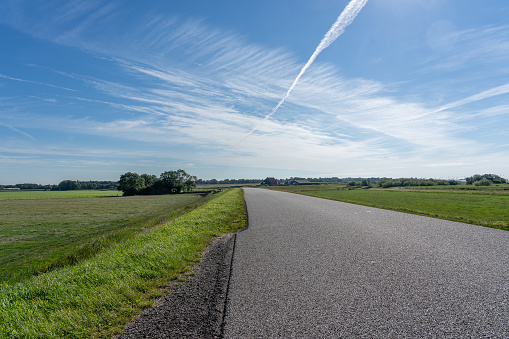 Low angle shot of a empty road that disappears at the horizon in a rural landscape and under a blue sky