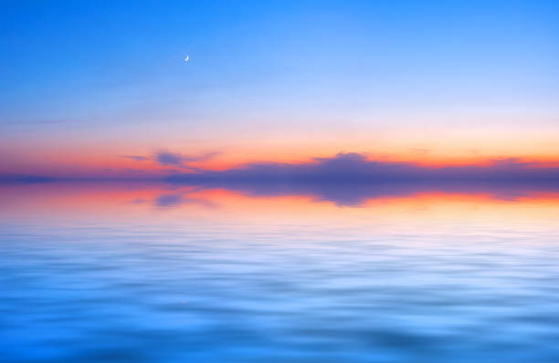 istock Sunset sky panorama with young moon above water surface 1267024466
