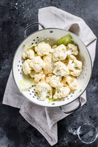 istock Washed fresh cauliflower cut into pieces in a colander. Black background. Top view 1267031452
