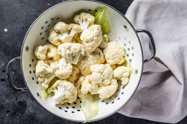 istock Washed fresh cauliflower cut into pieces in a colander. Black background. Top view 1267031572