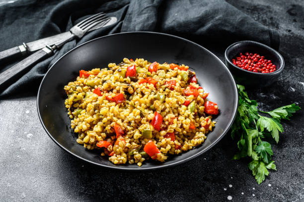 istock Bulgur with vegetables and meat on a plate. Black background. Top view 1267039175