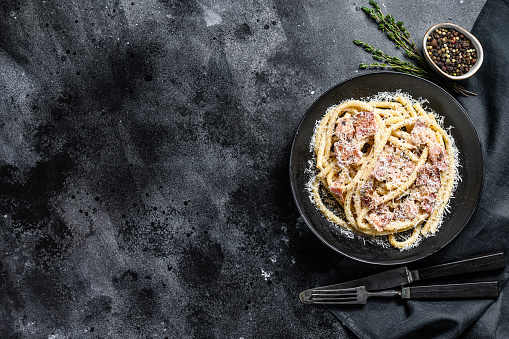 Pasta Carbonara on black plate with parmesan, bucatini. Black background. Top view. Copy space.