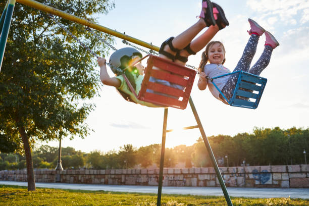 meninas alegres balançando juntos em um balanço em um parque - swinging sister family child - fotografias e filmes do acervo