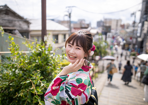 Happy young woman in yukata looking over shoulder on street