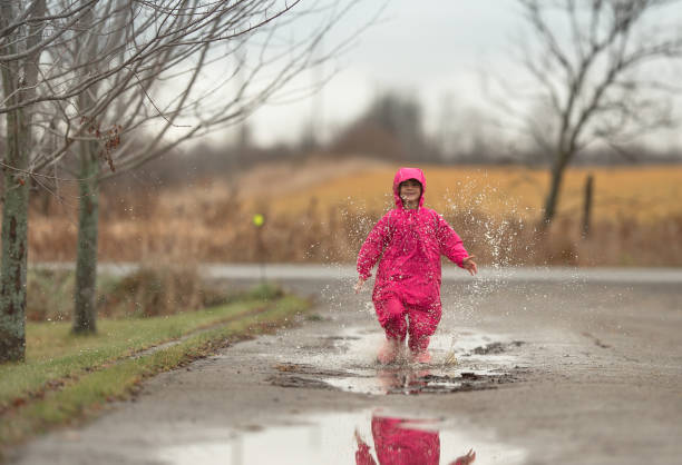 istock Girl running through rain puddles in pink rain suit 1267048111