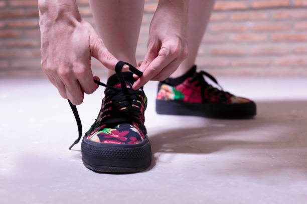 istock Young woman standing tying her colourful canvas shoes 1267050662