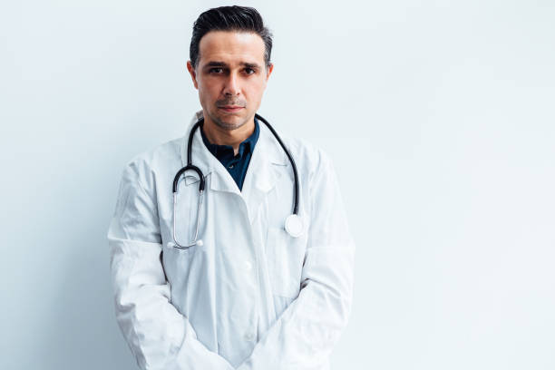 istock Black haired doctor wearing white coat and stethoscope looking at camera, on white background. Medicine concept 1267053512