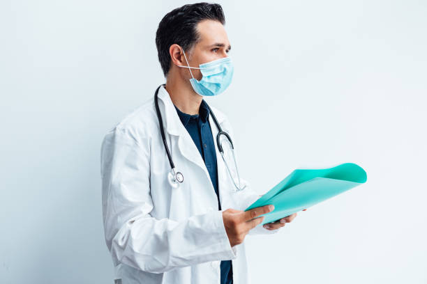 Doctor in surgical mask, white coat, stethoscope and blue folder with a report in his hand. Medicine concept stock photo