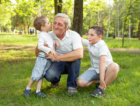 Joyful nice loving boys hugging and kissing his grandfather while expressing his feelings. Happy grandpa and children have fun and play together on beautiful sunny day. Summer fun. Family concept