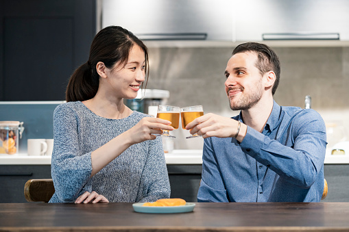 young man and woman toasting with glass of beer at home