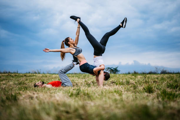 Three young Caucasian athlete people practicing acroyoga on meadow.