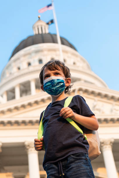 国会議事堂の前で保護フェイスマスクとバックパックを身に着けている深刻な小さな男子生徒 - little boys preschooler back to school backpack ストックフォトと画像